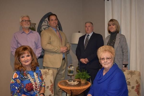 Six people posing indoors around a small table with a potted plant.