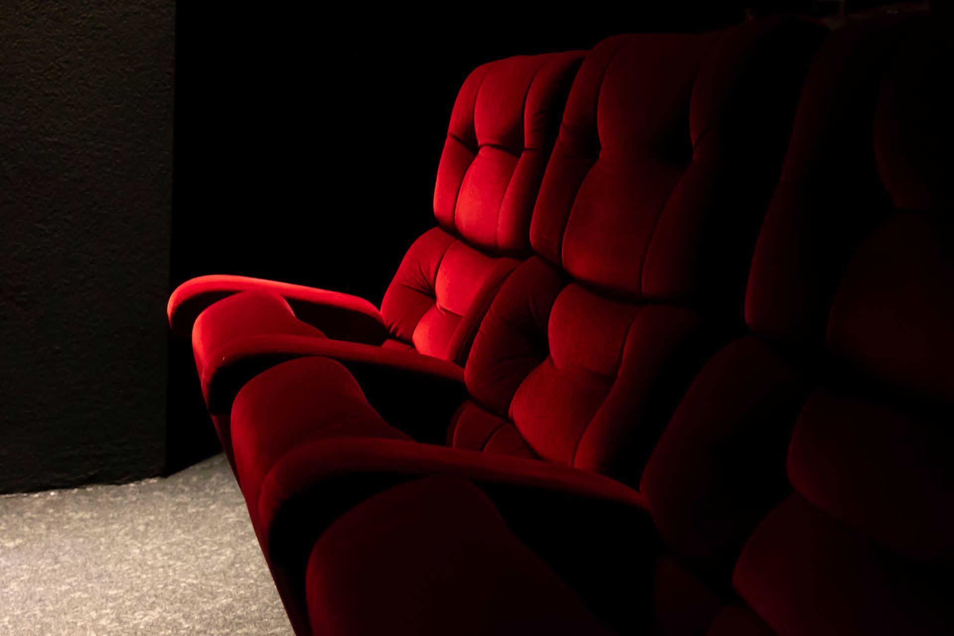 A red couch is sitting in a dark room in a movie theater.