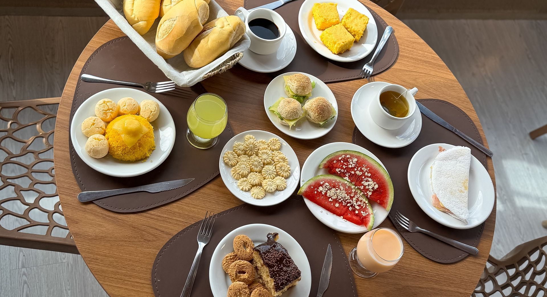 Vista de cima para baixo de uma mesa com diversos pratos de café da manhã, xícaras de café, pão, frutas e doces.