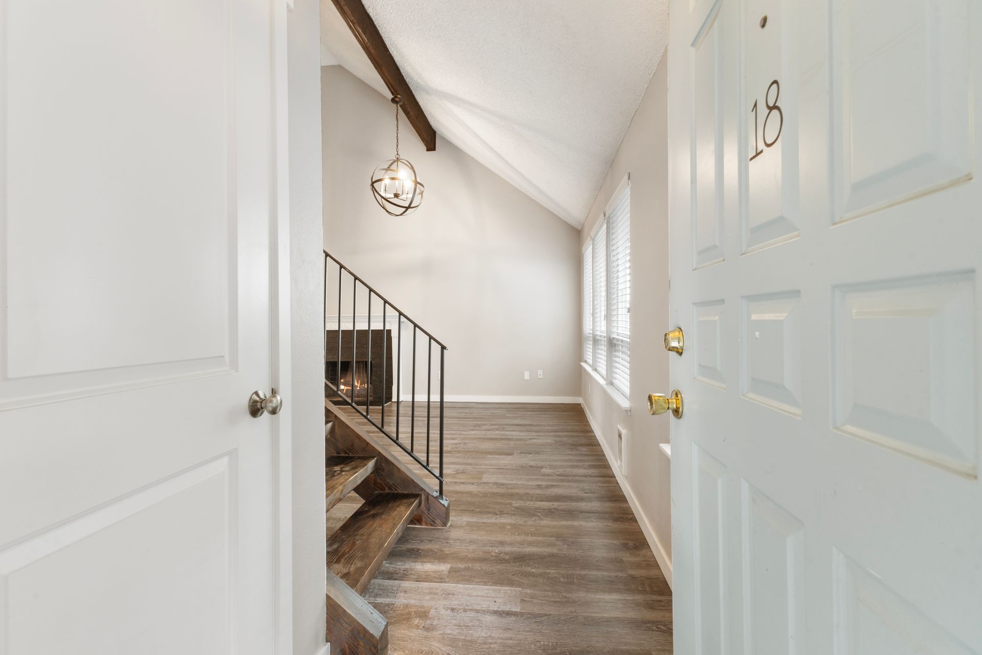 A white door is open to a hallway with wooden floors and stairs.