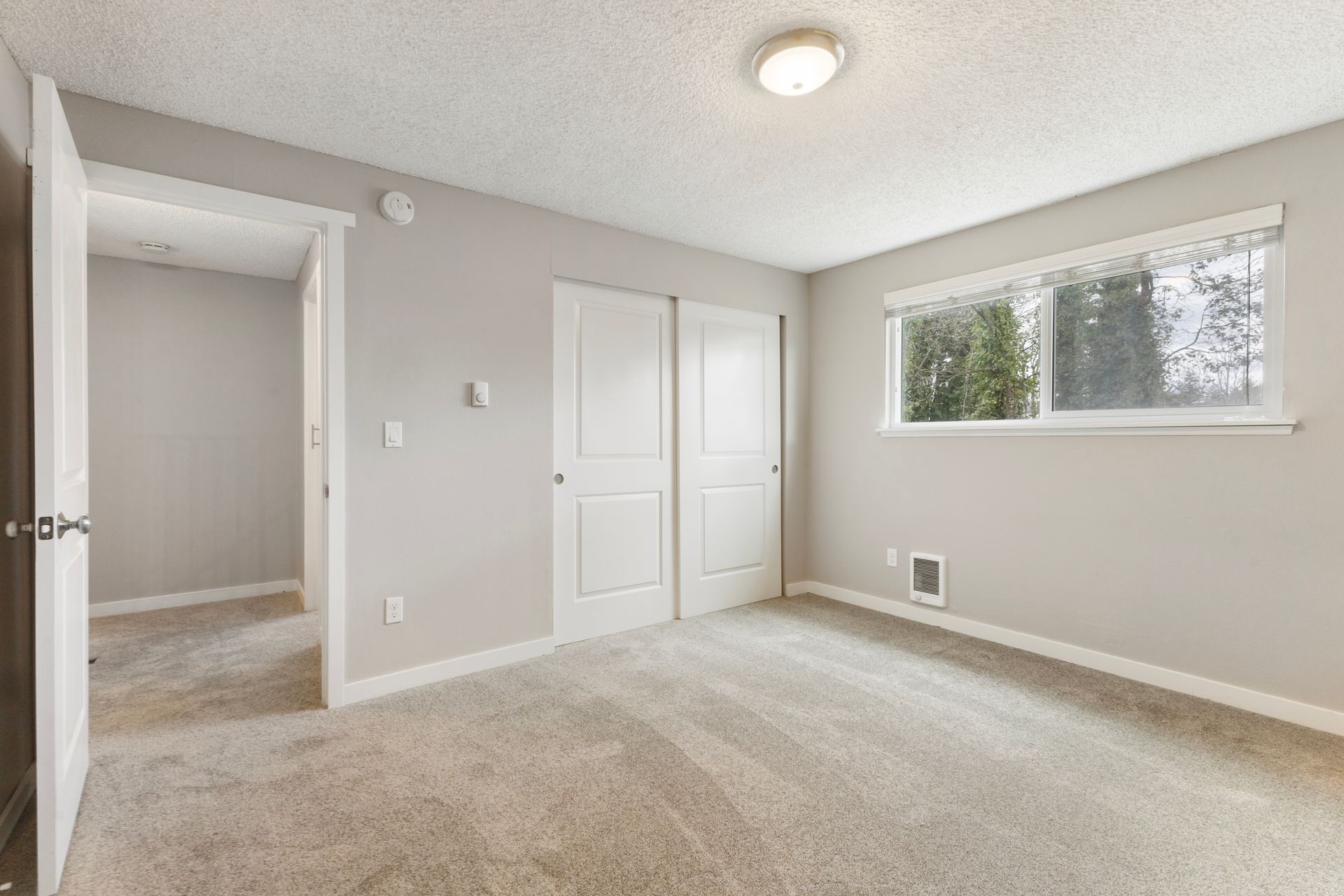 An empty bedroom with a carpeted floor and a window.