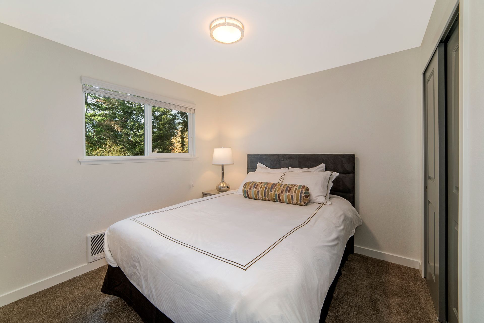 A bedroom with a bed , two windows and a lamp.
