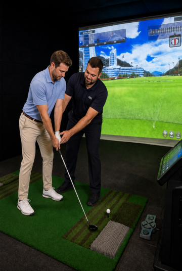 Golfer swinging a club on an indoor simulator with a large scenic screen behind him.