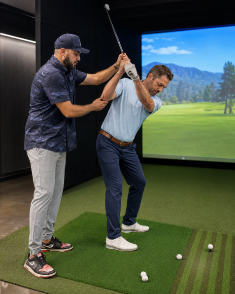 Golfer swinging a club on an indoor simulator with a large scenic screen behind him.