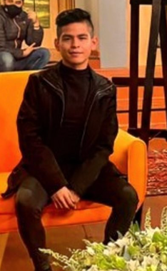 Un hombre vestido de negro se sienta en un sofá naranja, con las manos entrelazadas.