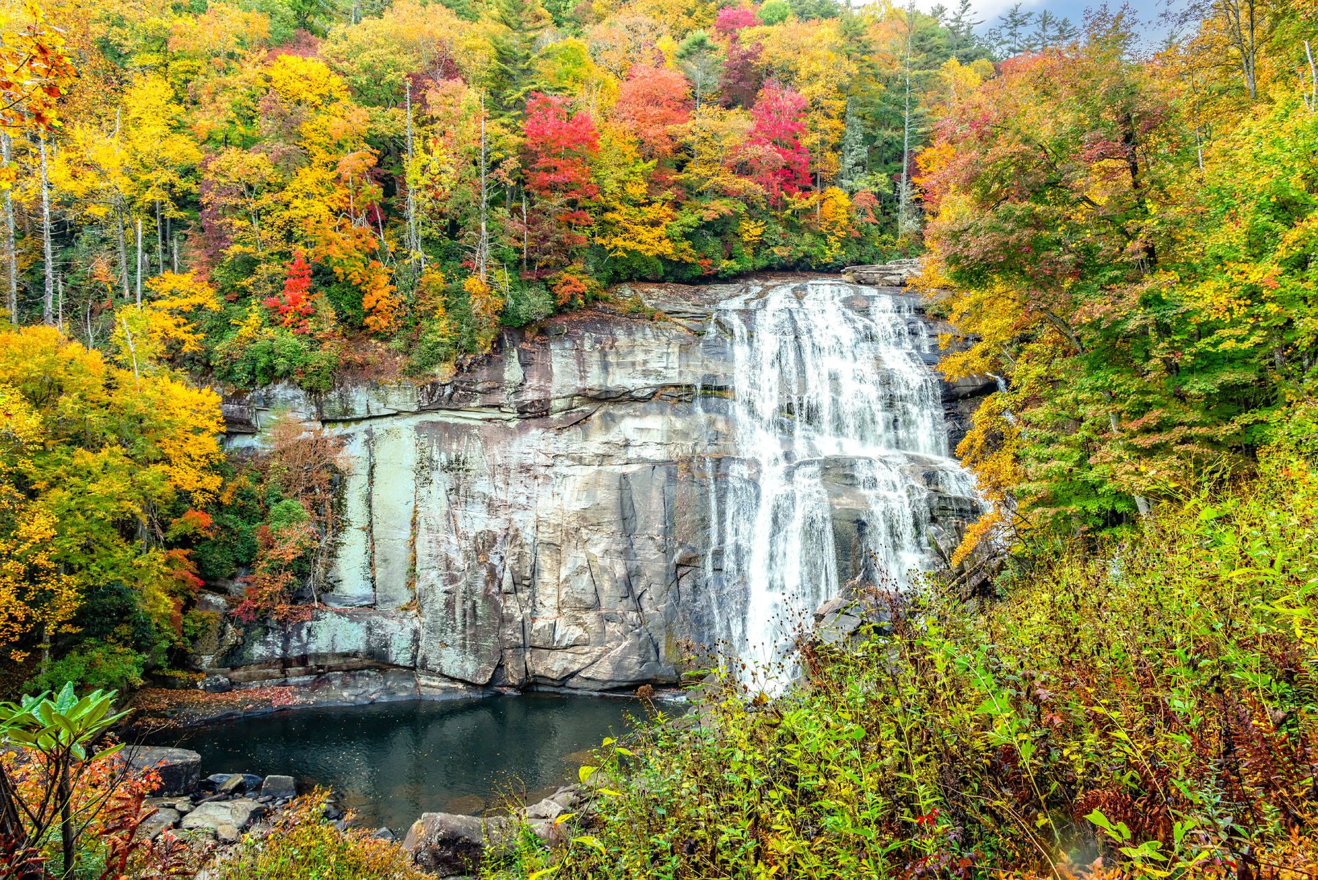 A waterfall in the middle of a forest surrounded by trees with autumn leaves.