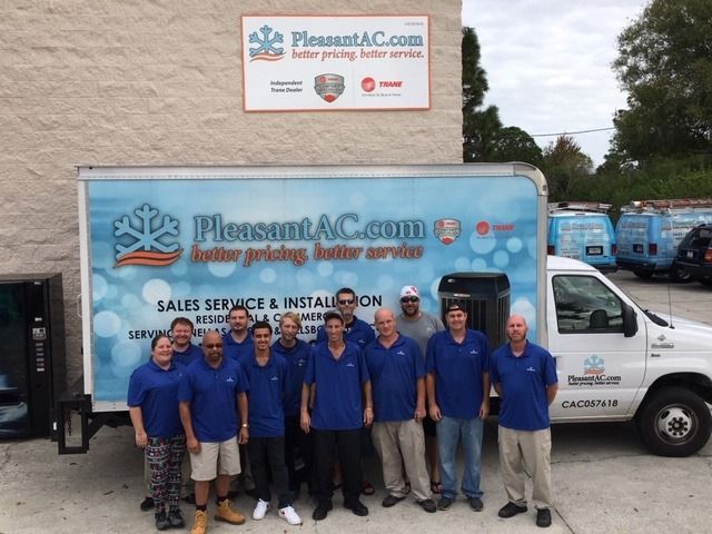 Pleasant AC team in blue shirts posing by a service truck outside their office