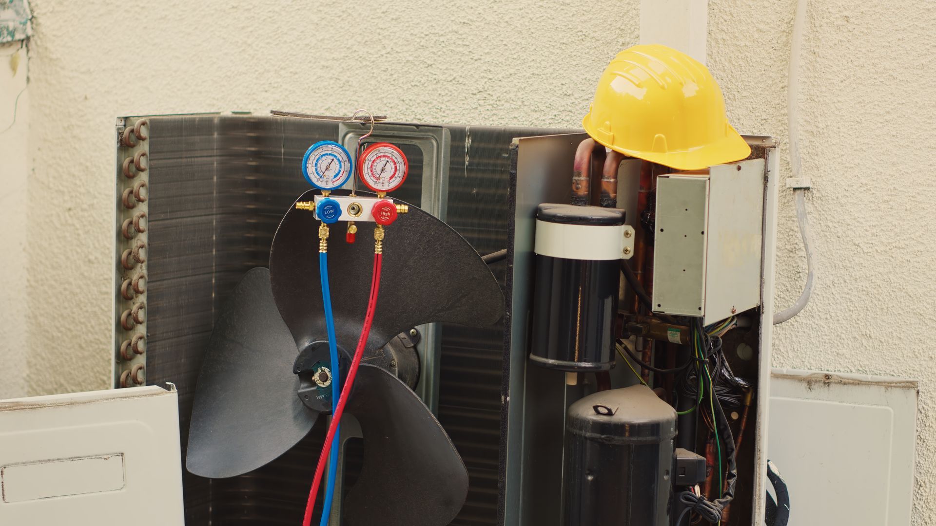 HVAC unit with gauges, colored hoses, wiring, and a yellow hard hat on top