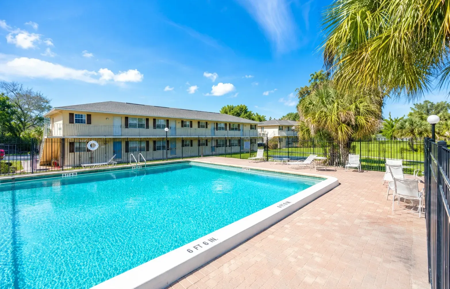 Outdoor swimming pool with lounge chairs and palm trees, adjacent to apartment buildings.