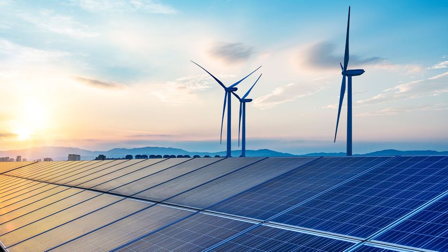 Solar panels in a field with wind turbines at sunrise under a blue sky.