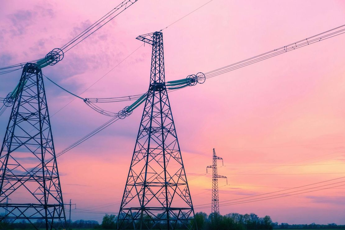 Power lines and transmission towers silhouetted against a pink sunset sky