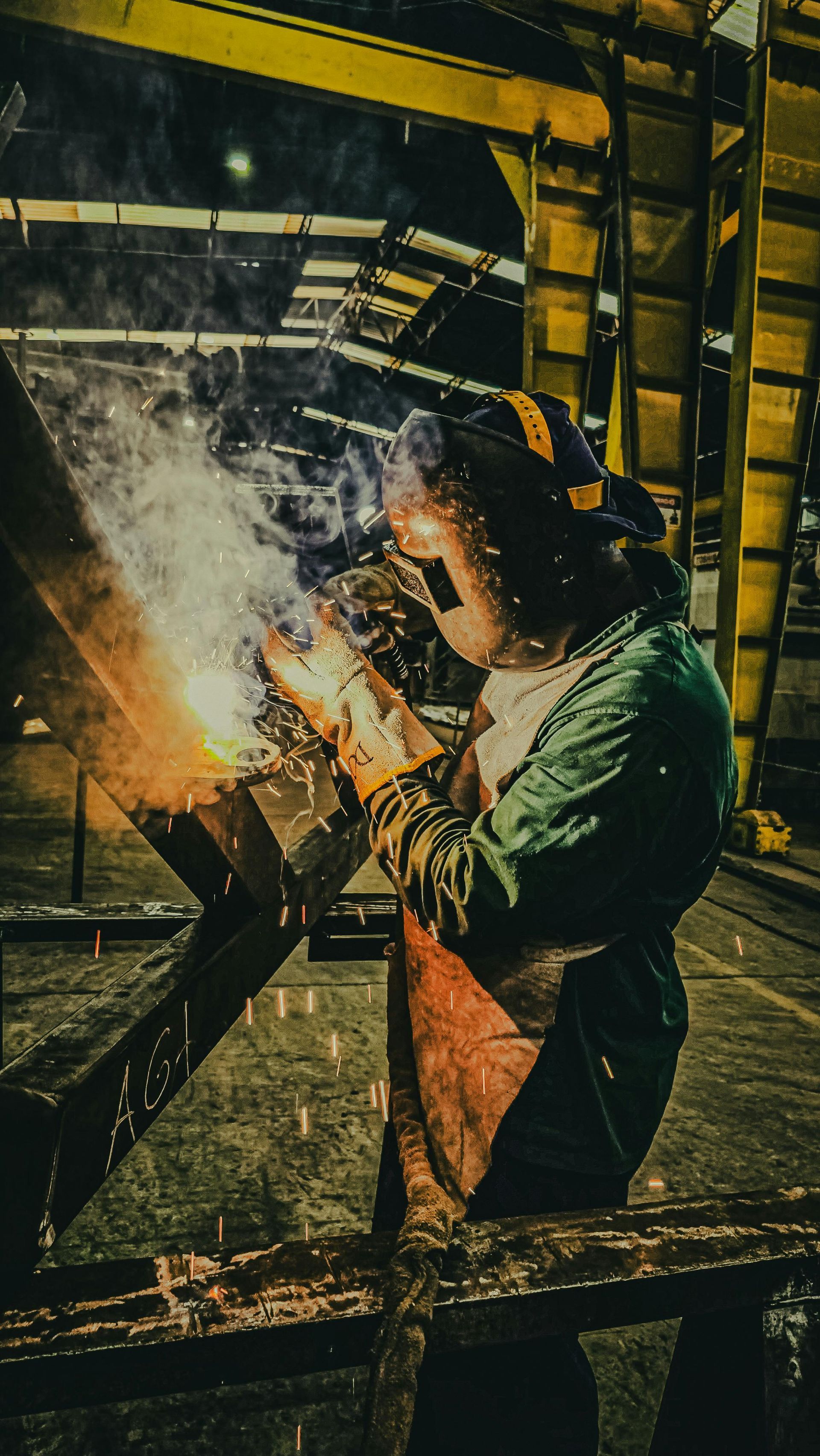Welder in protective gear sparks metal in a dim industrial workshop