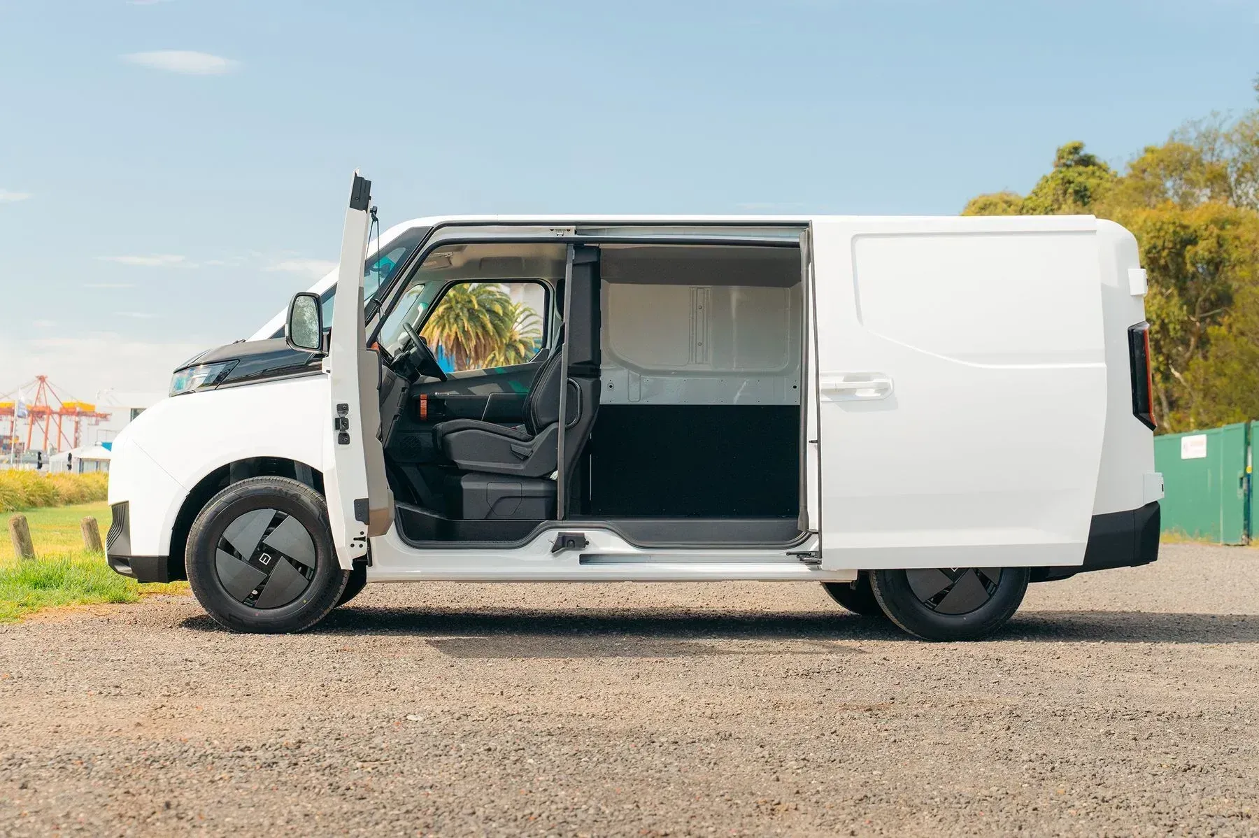 A side view of a white electric delivery van parked on a gravel surface with its sliding side door open.
