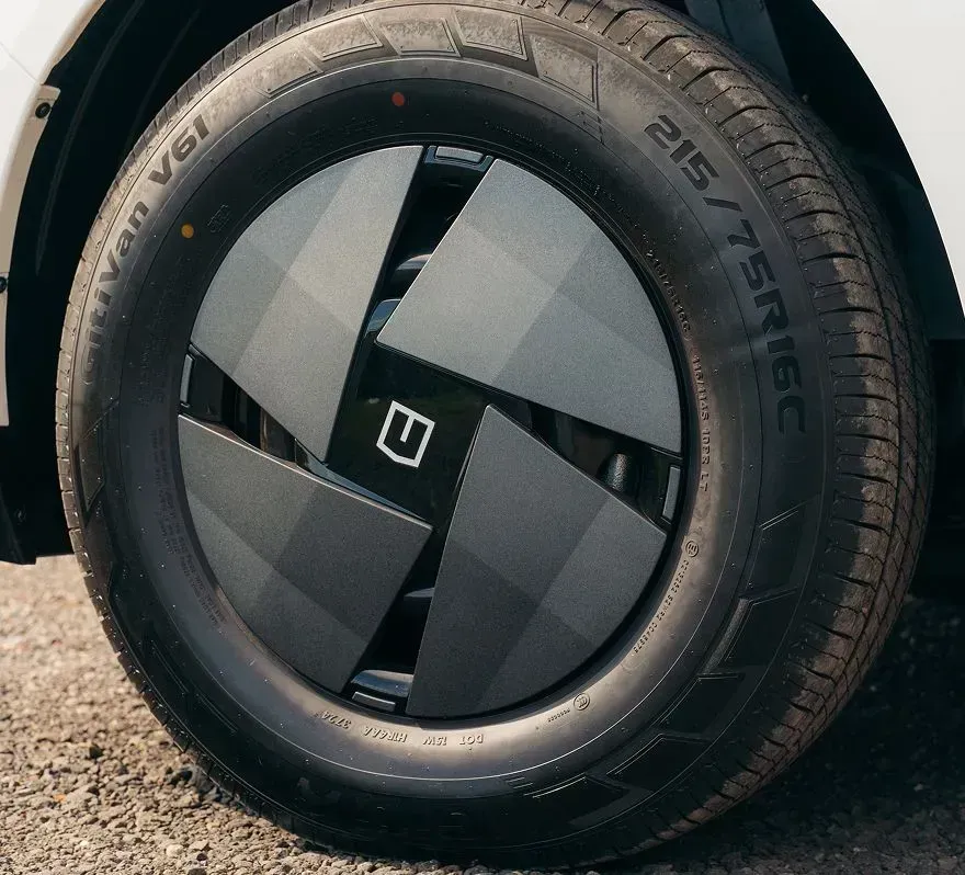 A close-up of a dark grey, geometric, aerodynamic wheel cover with a square logo, mounted on a 215/75R16C tire.