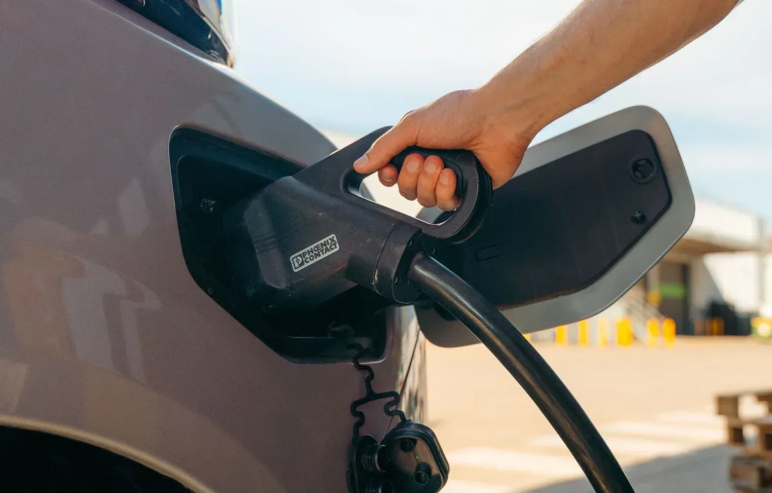 A person plugging a black charging cable into the port of a light purple electric vehicle outdoors.