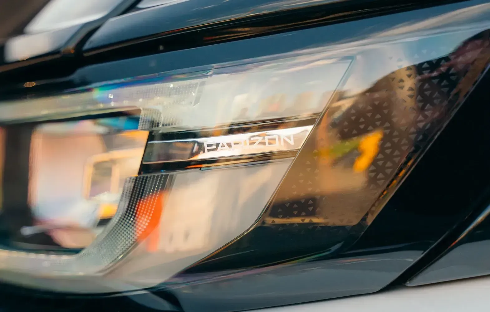 Close-up of a modern car headlight with a textured dark trim and a metallic logo strip inside the lens.