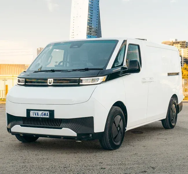 A white electric delivery van parked outdoors in front of a modern high-rise building.