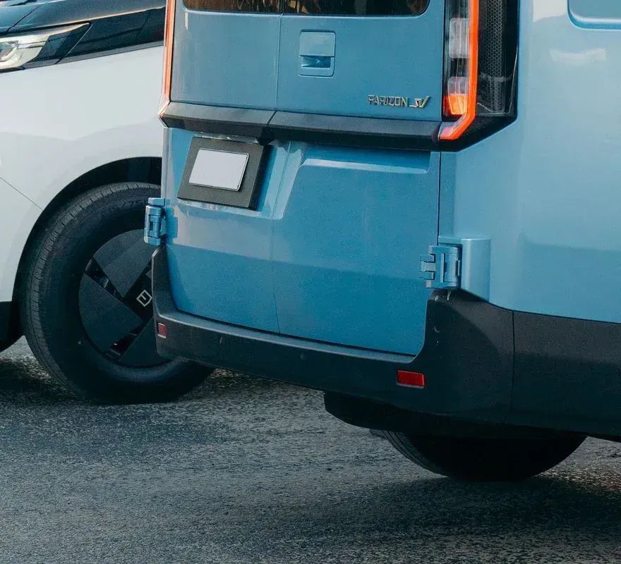 A light blue cargo van parked next to a white car on an asphalt surface.