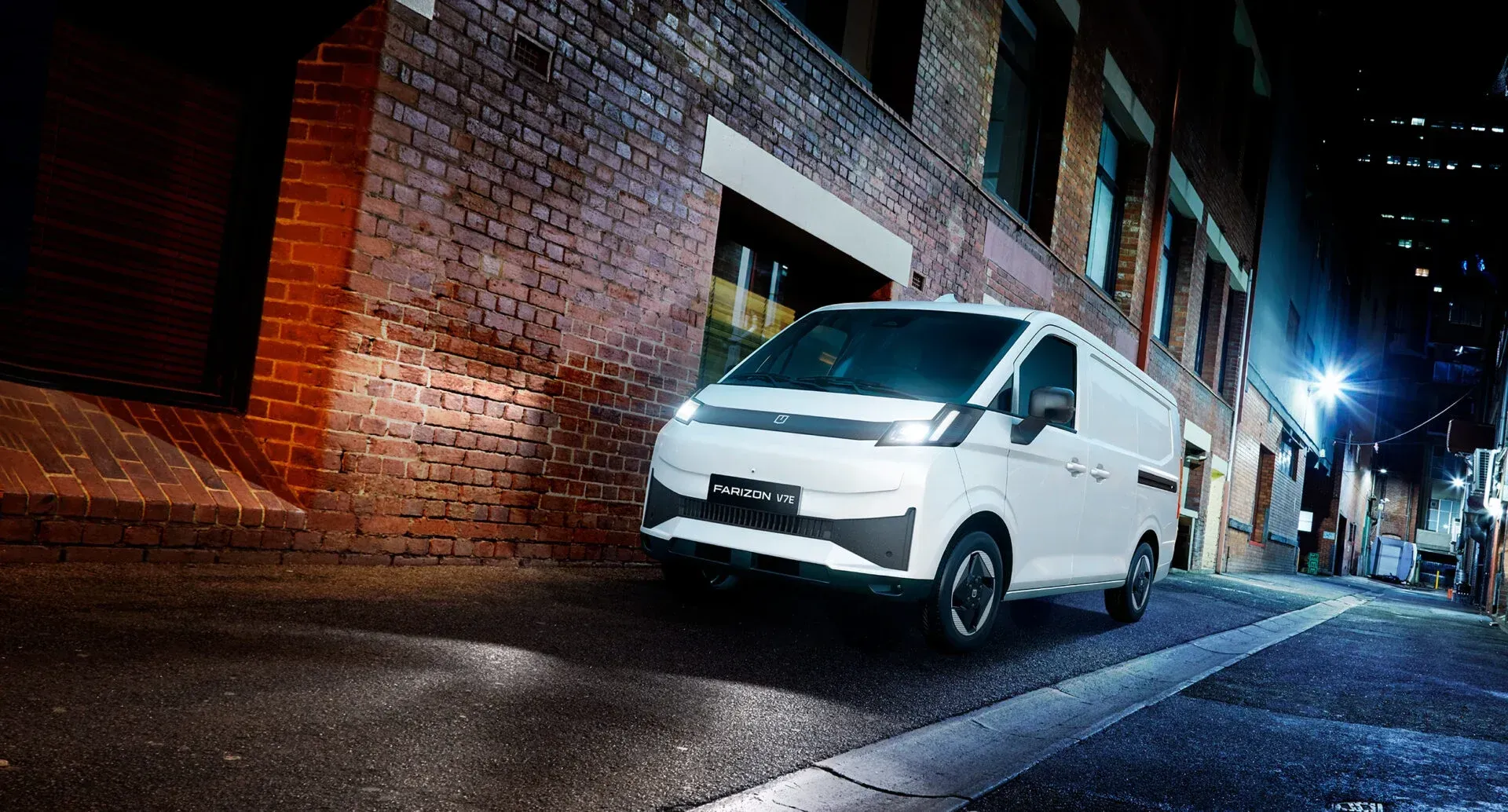A white cargo van parked on a narrow brick-walled alley street at night.