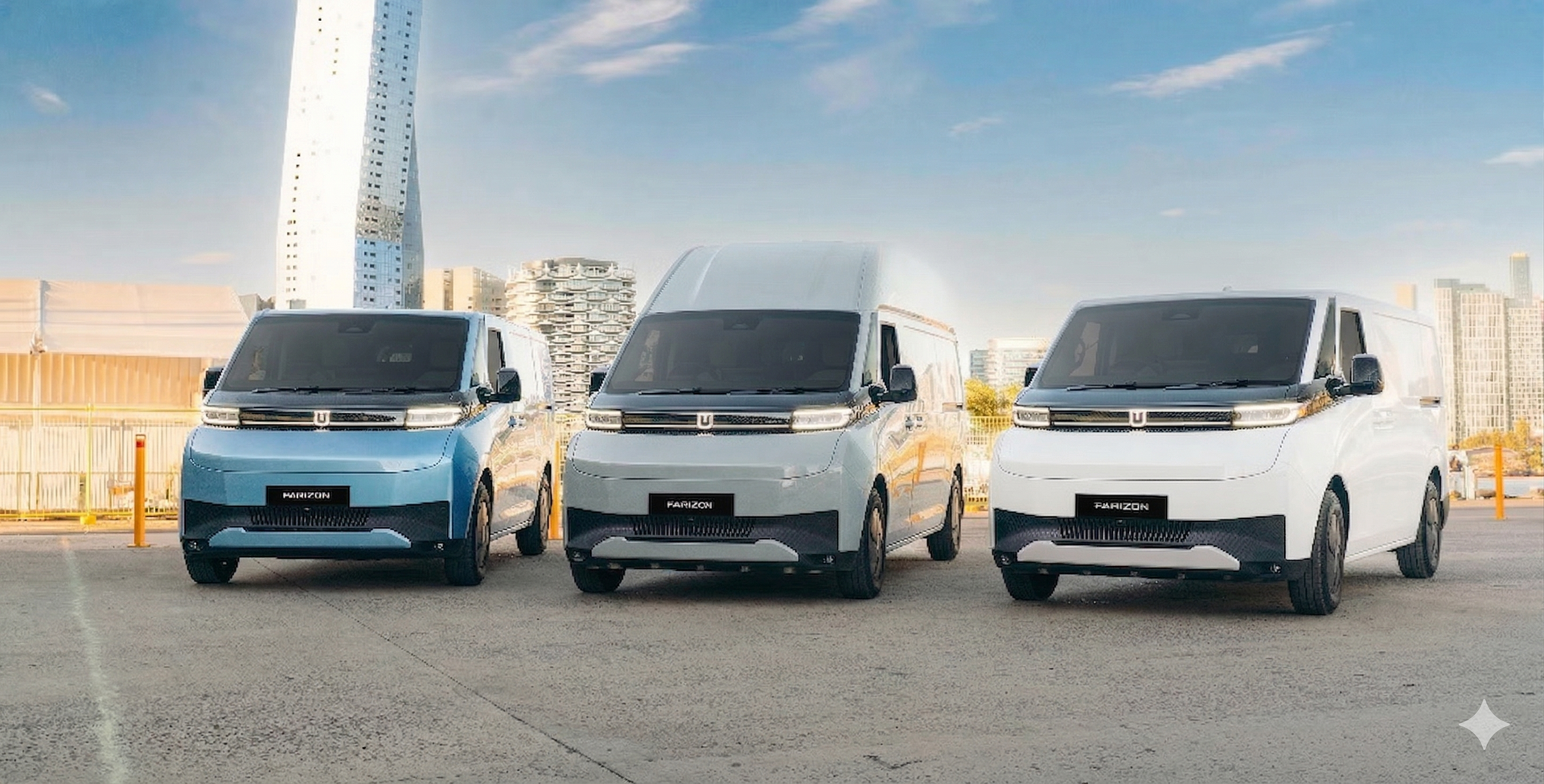 Three modern electric vans—light blue, gray, and white—parked side-by-side in a paved lot with a city skyline backdrop.