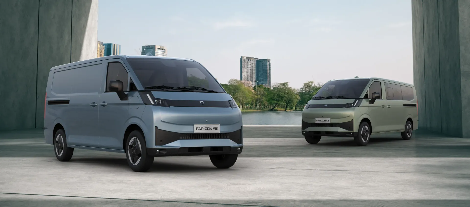 Two modern, boxy vans—one silver and one sage green—parked on a concrete plaza with a lake and buildings in the background.