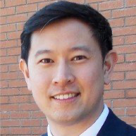 Smiling man in a dark suit before a brick wall