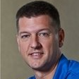 Portrait of a man with short dark hair wearing a blue shirt against a neutral background
