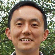 Close-up portrait of a smiling person outdoors with trees in the background