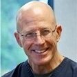 Smiling bald man with glasses wearing a dark jacket against a light background
