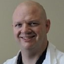 Smiling bald man in a white coat against a plain background