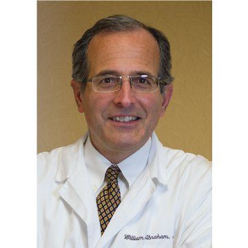 Portrait of a smiling man in a white lab coat, wearing glasses and a patterned tie.