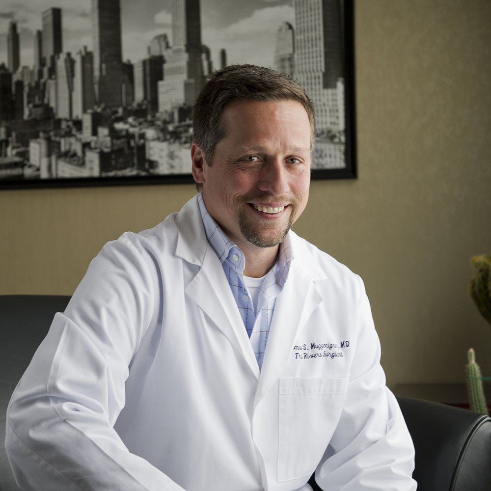 Doctor in a white lab coat smiling in an office with a cityscape photo behind him