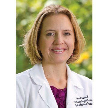 Woman in a white lab coat smiling outdoors against a blurred green background