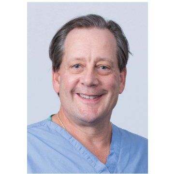 Smiling man in blue medical scrubs against a light gray background