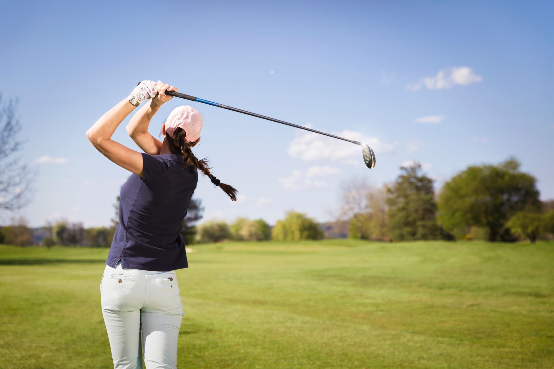 Golfer swinging a club on a sunny course with green fairway and blue sky