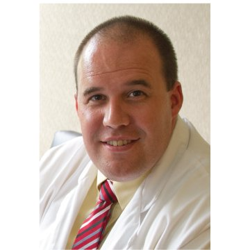Portrait of a smiling man in a white shirt and red striped tie against a light background