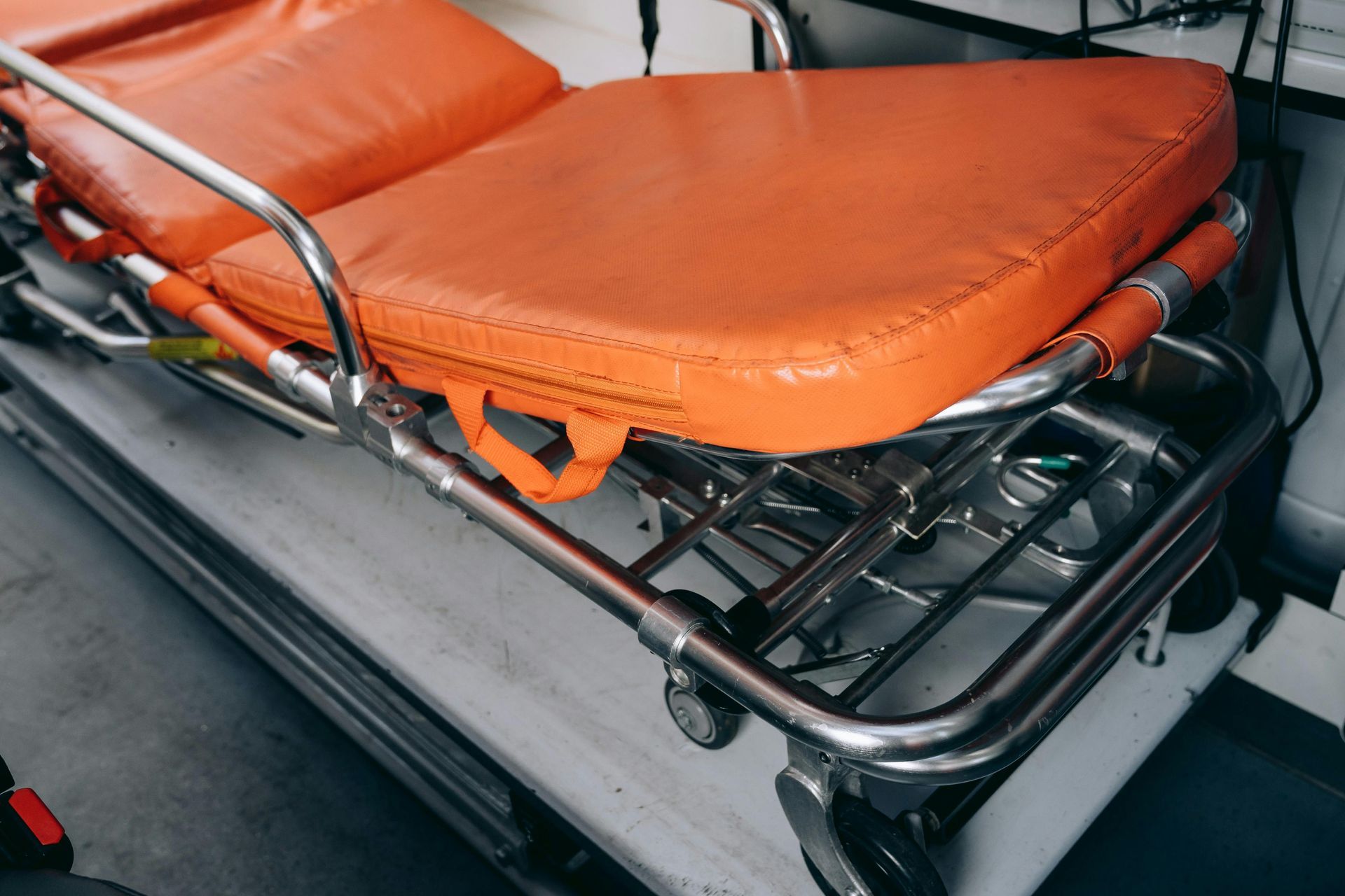 Orange stretcher mattress on a metal ambulance gurney inside a vehicle
