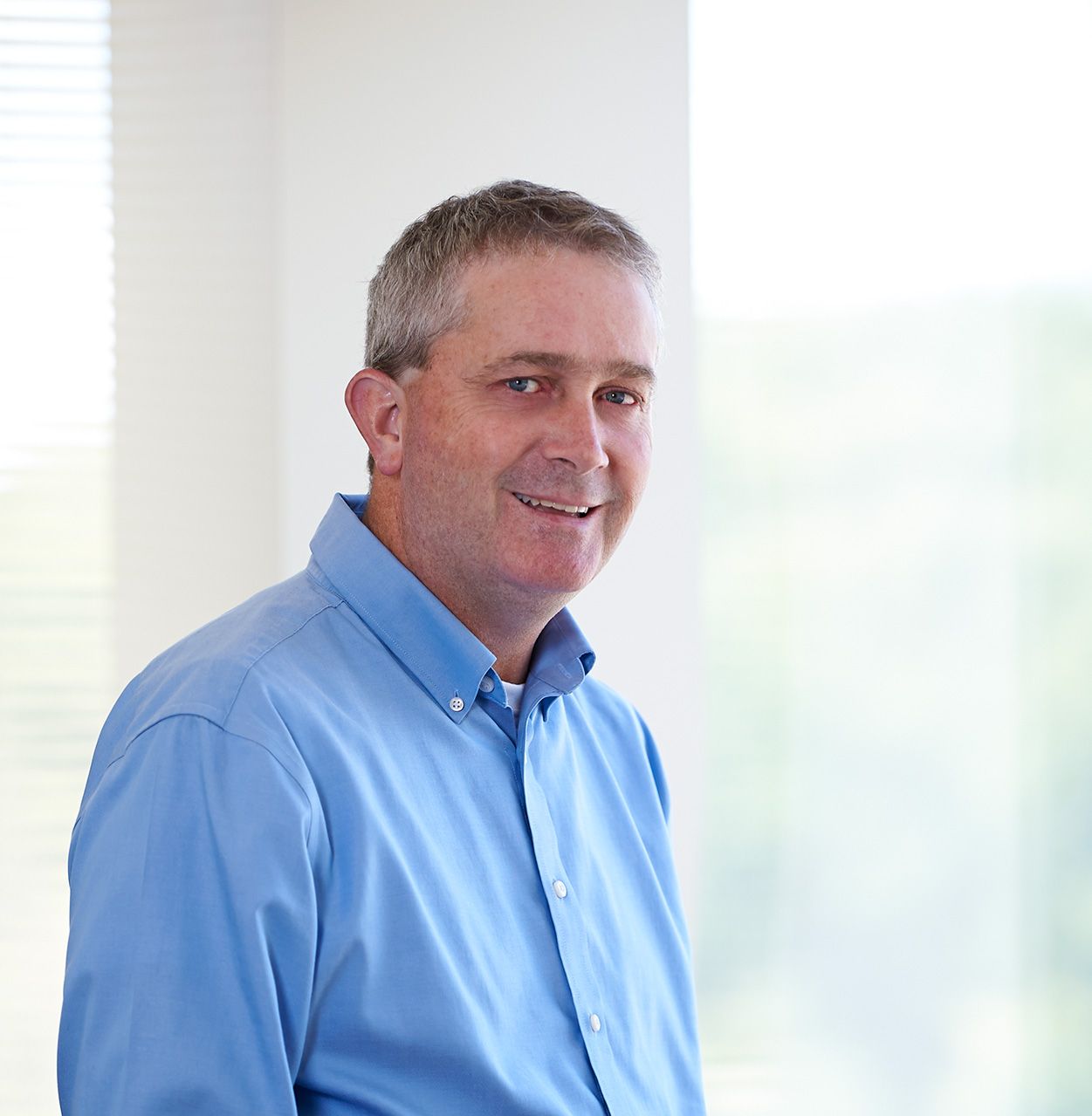 Smiling man in a light blue shirt standing by a bright window