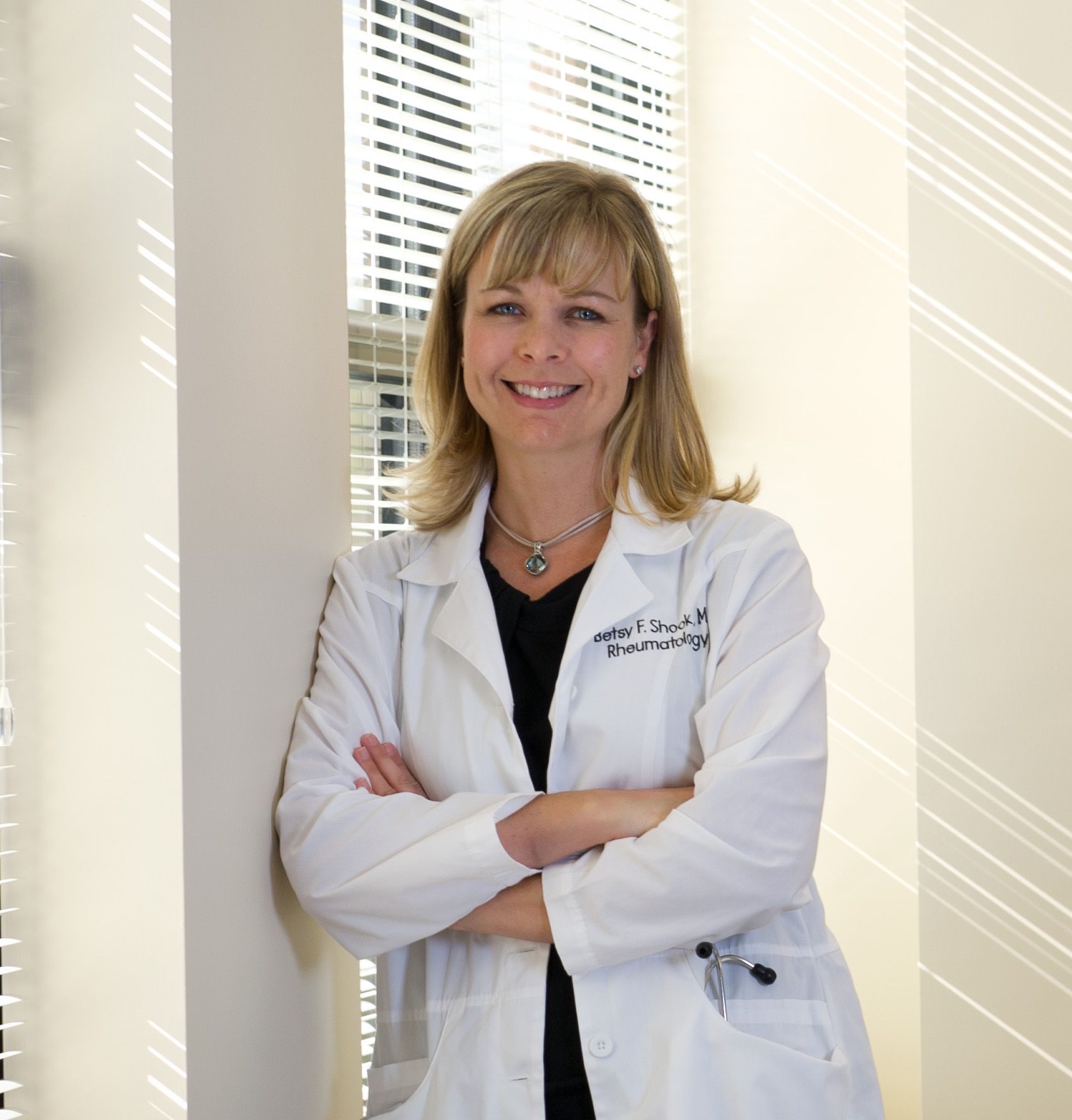 Smiling doctor in white coat standing with arms crossed in a bright office