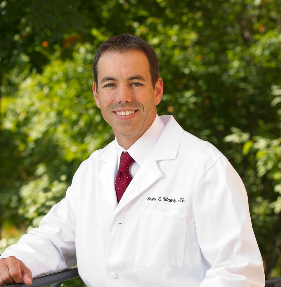 Smiling doctor in white coat and red tie standing outdoors by greenery
