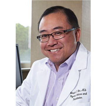 Smiling doctor in glasses and white lab coat, seated in an office.