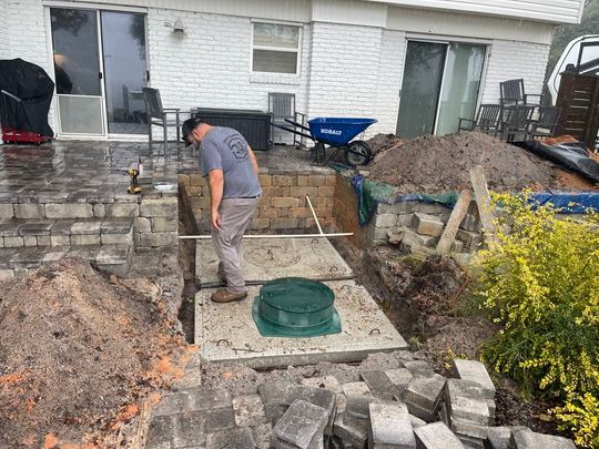 A man is working on a septic system in the backyard of a house.