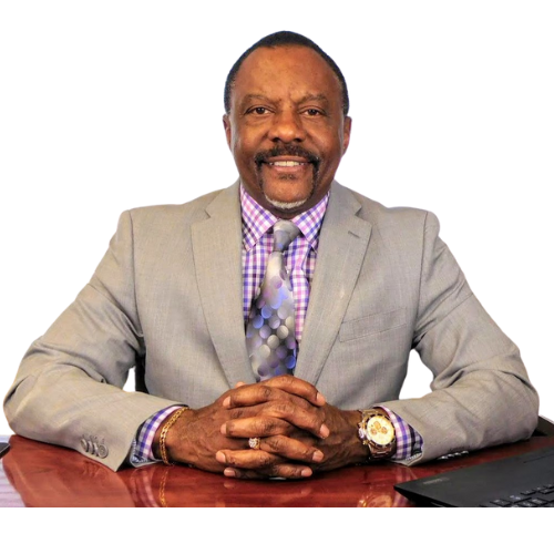 Man in a light gray suit smiling at a desk against a white background.