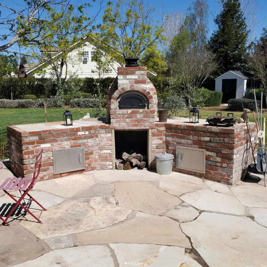 A kitchen with a sink and a grill on a brick patio.
