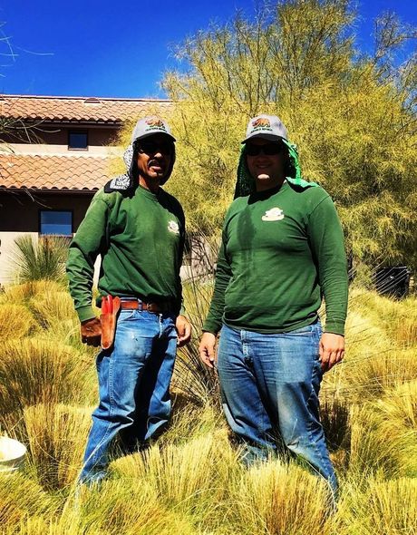 Two men are standing in a field of tall grass in front of a house.