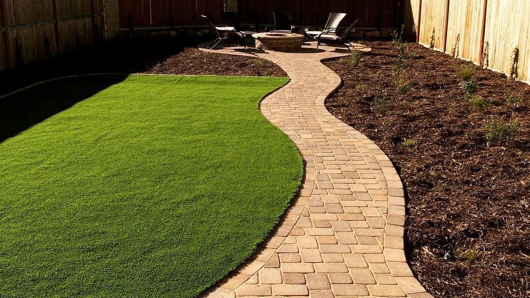 A brick walkway leading to a fire pit in a backyard.