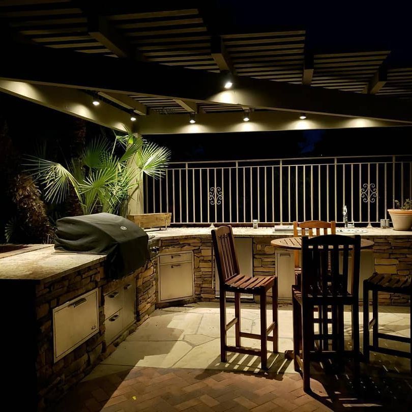 A patio with a table and chairs and a grill at night