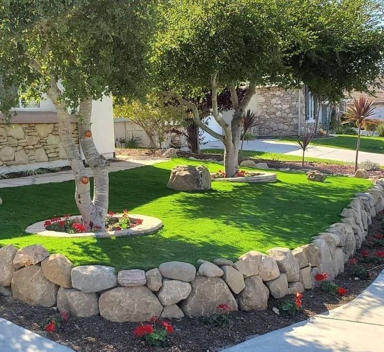A stone wall surrounds a lush green yard with trees and flowers