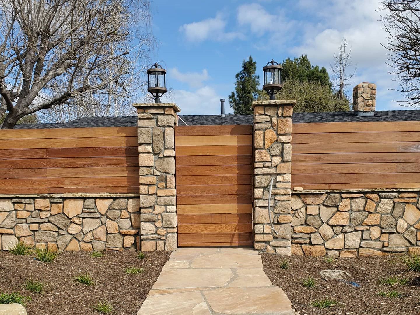 A wooden gate is surrounded by stone pillars and a stone wall.