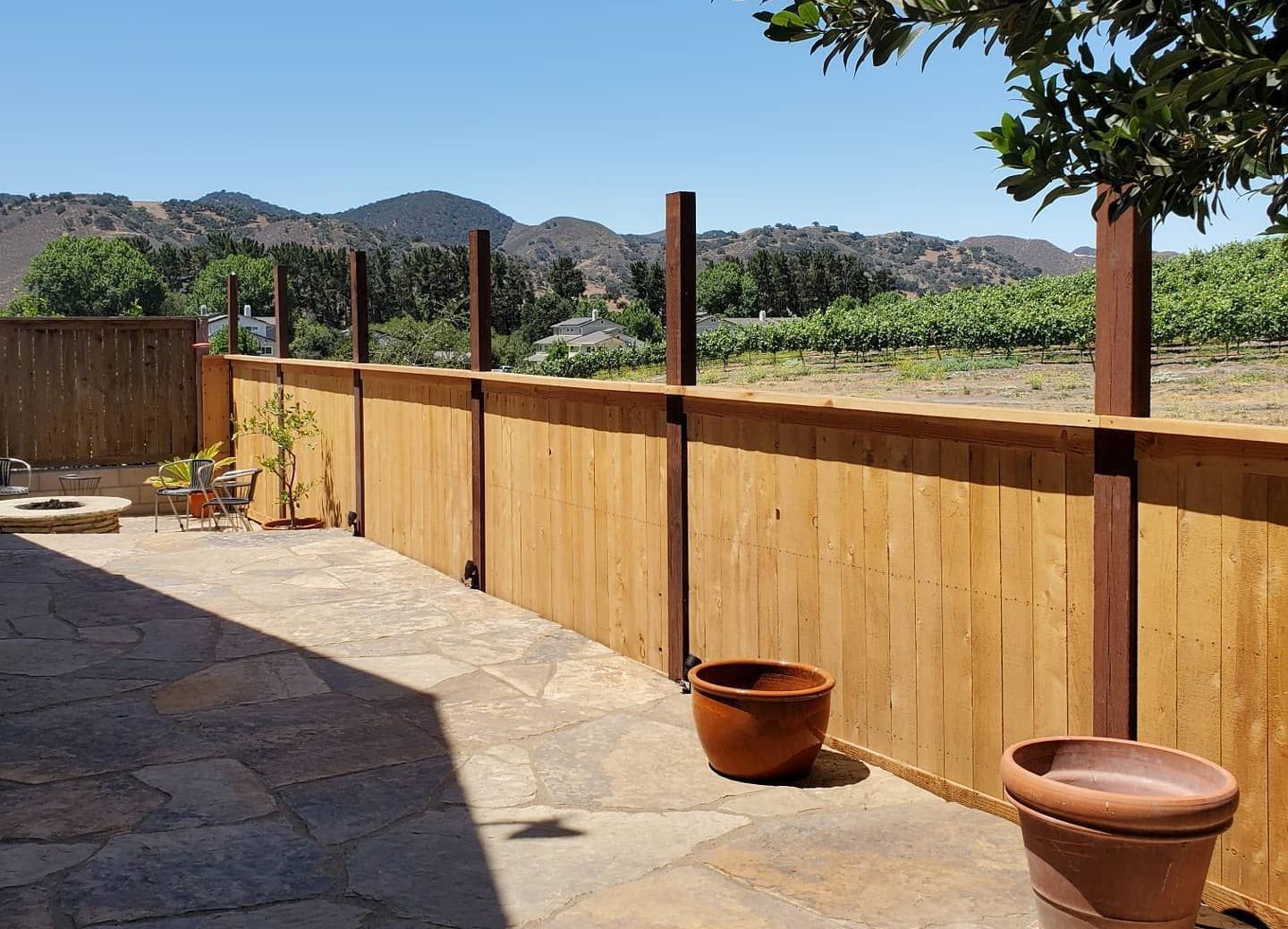A wooden fence surrounds a patio with a view of a vineyard.